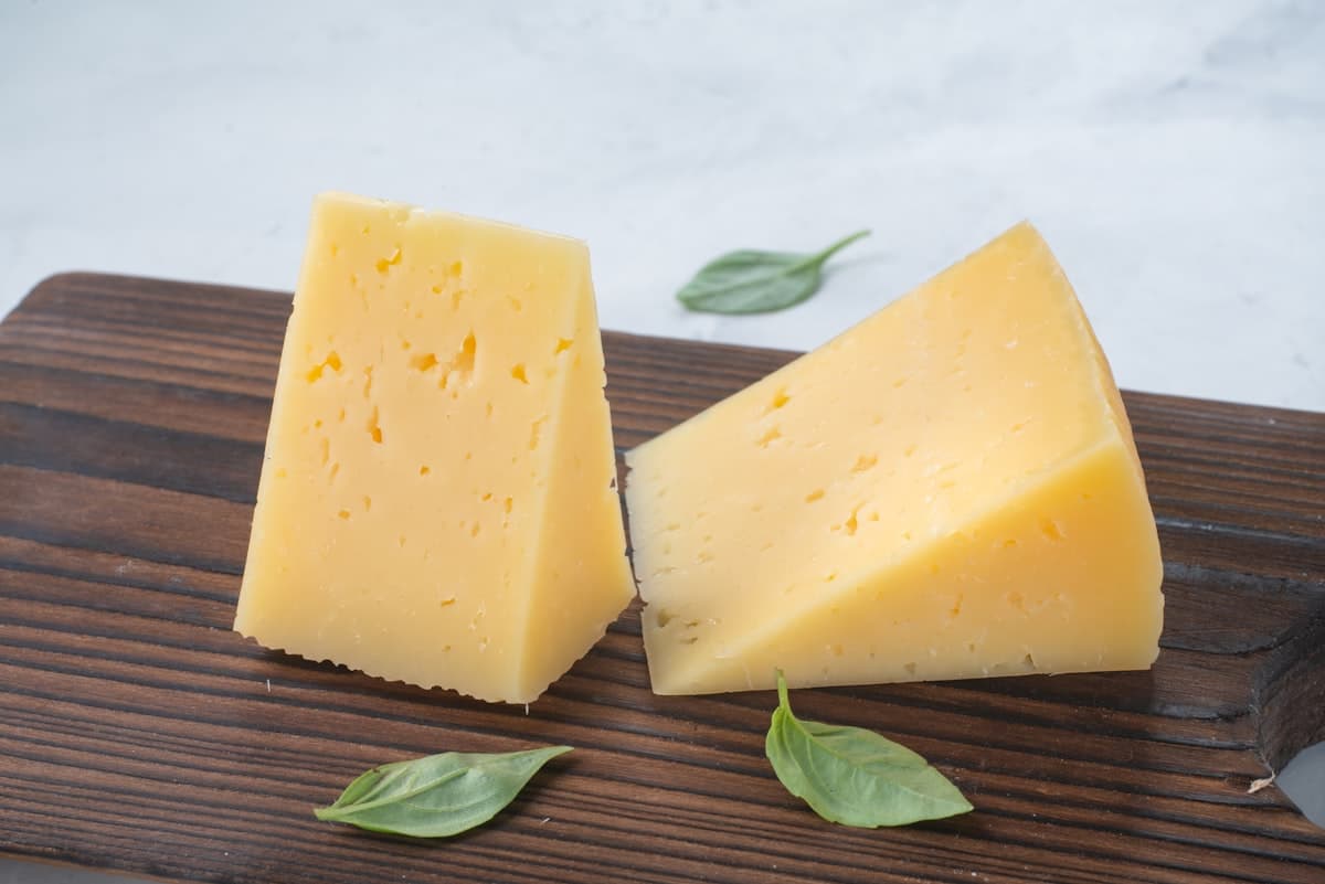 Deux quartiers de fromage à pâte dure sur une planche de bois